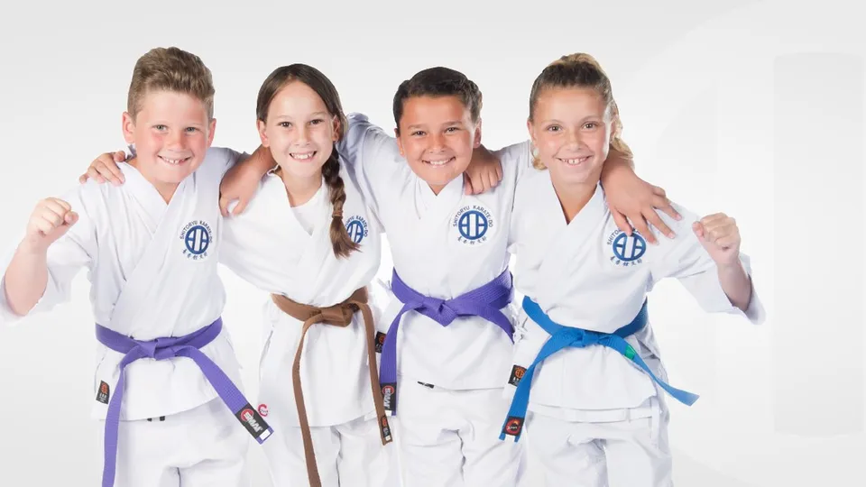 Four smiling children in white karate uniforms with purple, brown and blue belts