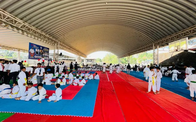 Young karateka competing on red and blue mats under a large hall roof